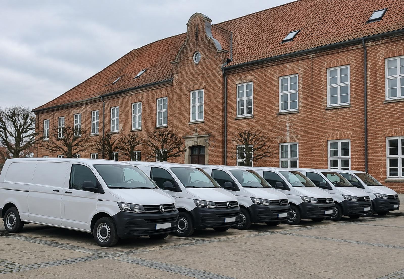 Række af hvide servicebiler parkeret foran en dansk kommunal bygning